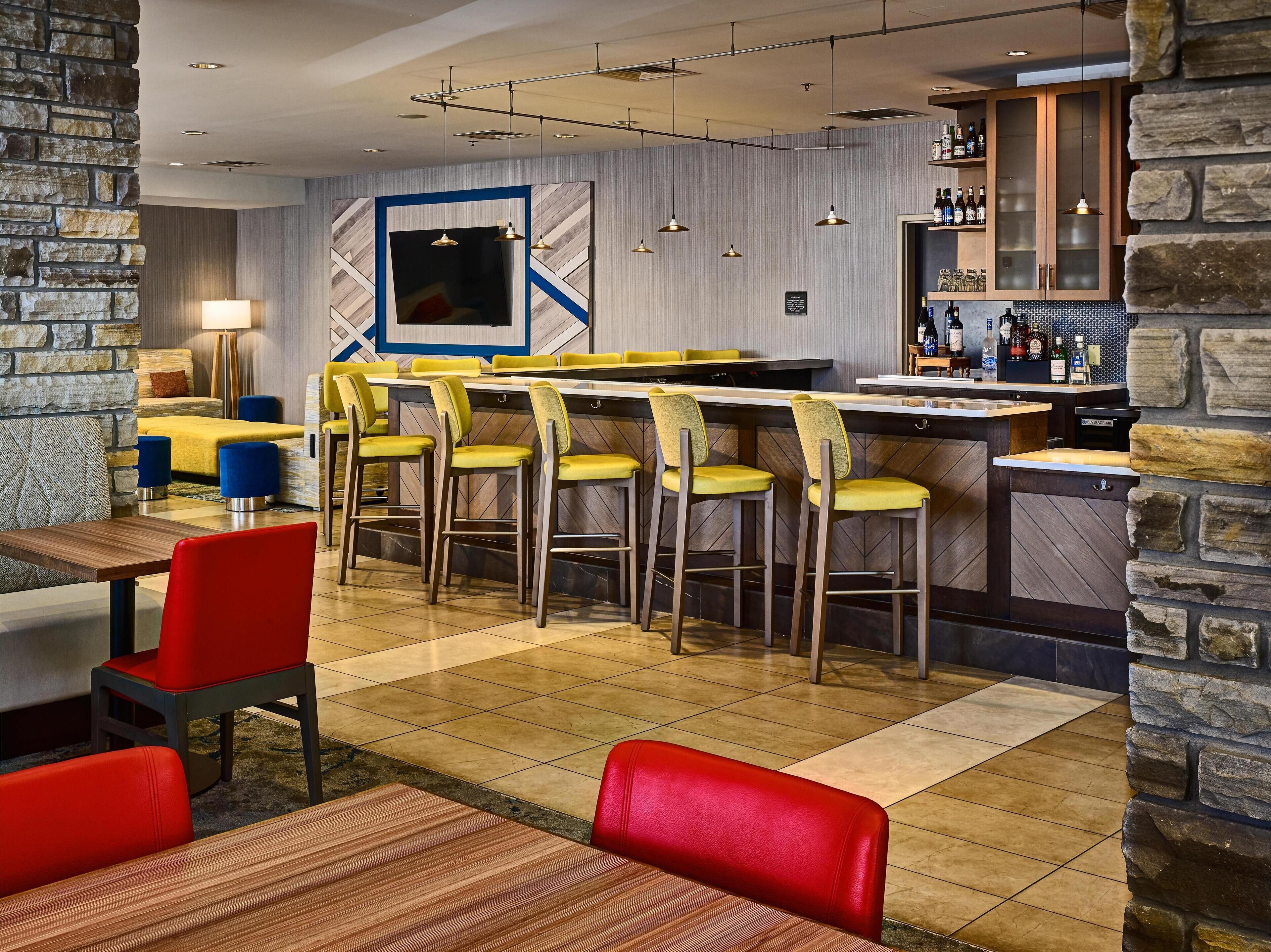 Un bar moderno con una pared de acento de piedra, una barra y una zona de estar con sillas amarillas y rojas.