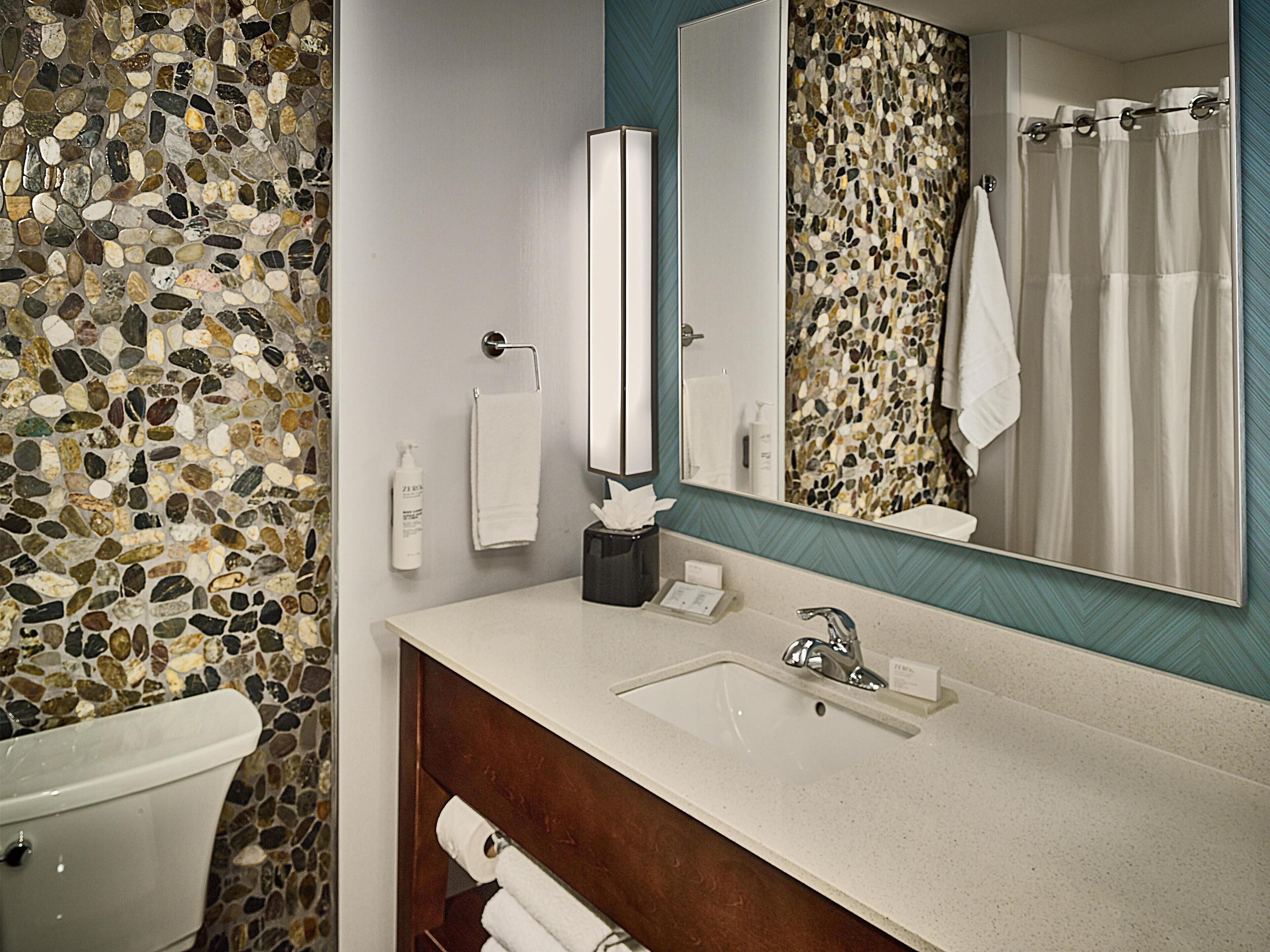 Un baño con pared de mosaico de piedra, un lavabo blanco, un espejo y una cortina de ducha.
