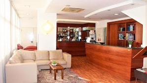 A modern hotel lobby with a sofa, coffee table, and a wooden reception desk. - Hotel Santa Lucia (Bastia Umbra)