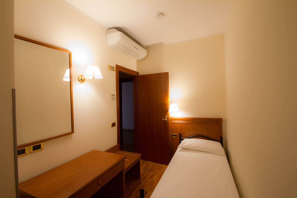 Una habitación de hotel con un escritorio de madera, una cama, un espejo y dos lámparas de pared.
