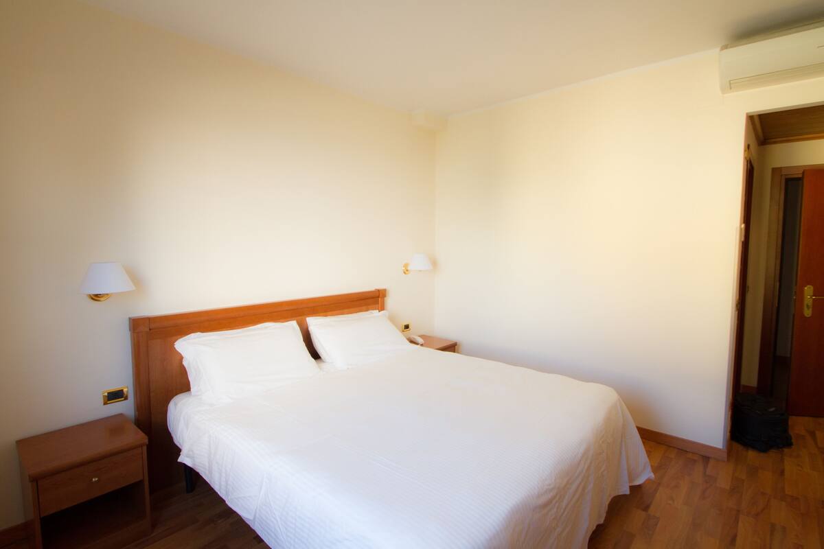 Una cama bien hecha con sábanas blancas, un cabecero de madera y dos lámparas de noche.