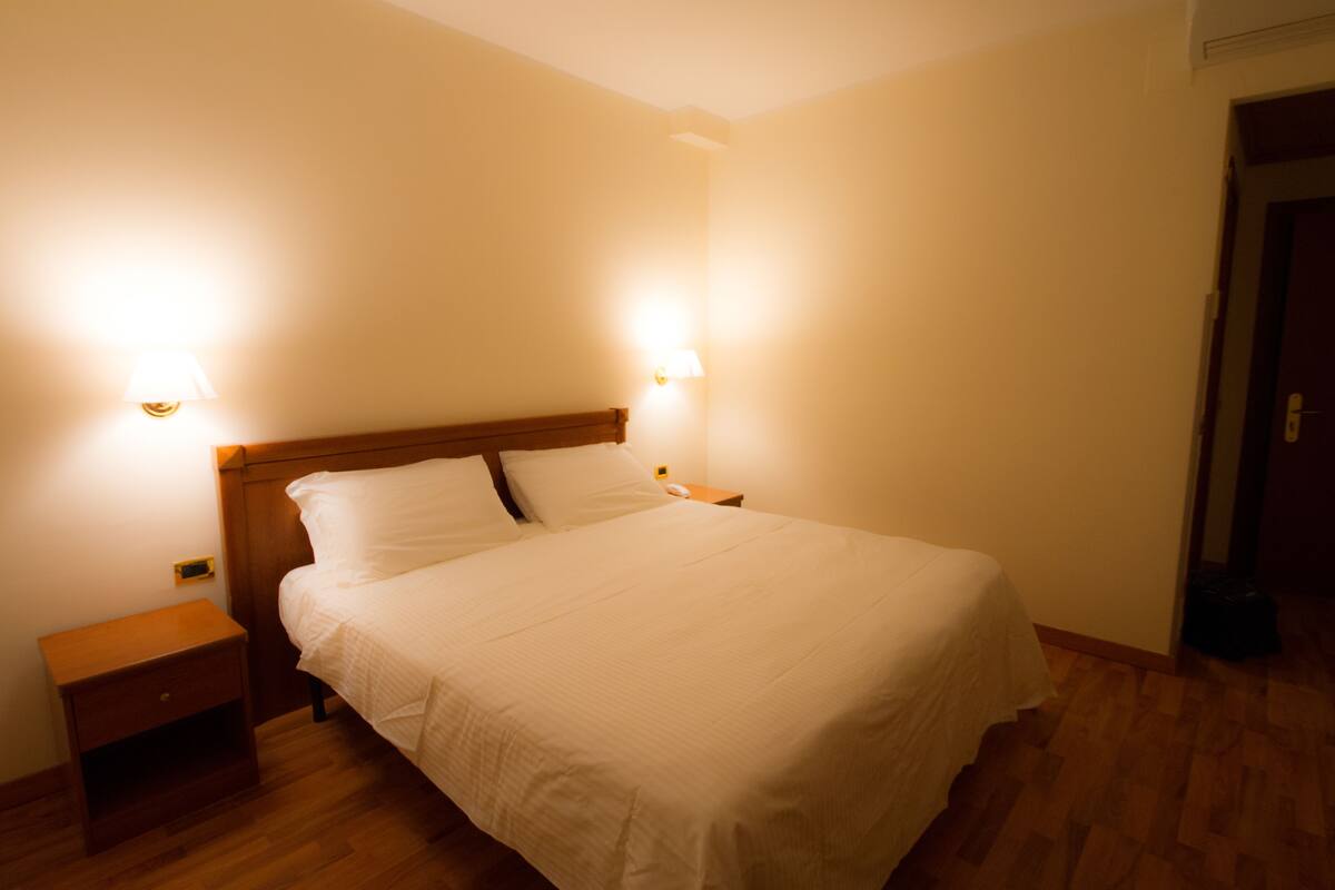 Una cama bien hecha con cabecera de madera en una habitación con dos lámparas de noche.