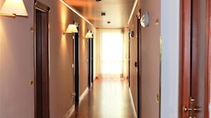 A hotel hallway with doors on both sides, overhead lighting, and a window at the end. - Hotel Santa Lucia (Bastia Umbra)