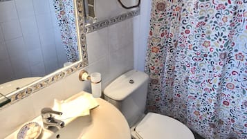 Un baño con lavamanos blanco, inodoro, espejo y cortina de ducha con estampado floral.