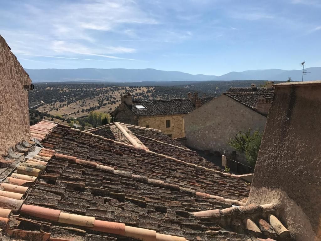 A view of terracotta-tiled rooftops with a valley and distant mountains in the background.