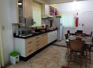 A compact kitchen with a dining area, featuring a microwave, sink, and various kitchen utensils. - Pousada Ares do Sul (Penha)