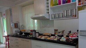 A kitchen with white cabinets, a black countertop, and various food items. - Pousada Ares do Sul (Penha)