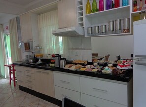 A kitchen with white cabinets, a black countertop, and various food items. - Pousada Ares do Sul (Penha)