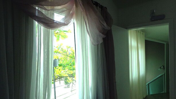 A room with a window covered by sheer curtains, a view of greenery outside, and a staircase leading to another area. - Pousada Ares do Sul (Penha)