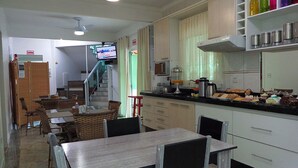 A kitchen with a dining area, a television, and a staircase leading to another room. - Pousada Ares do Sul (Penha)