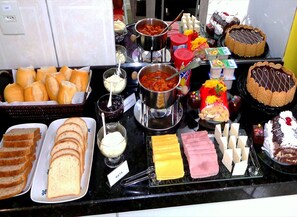 A buffet with various food items including bread, cheese, ham, and desserts. - Pousada Ares do Sul (Penha)