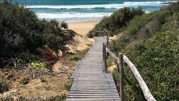 Une promenade en bois menant à une plage avec vue sur l’océan.