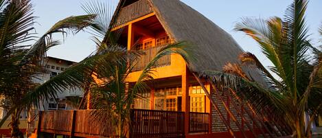 A thatched-roof building with a balcony, surrounded by palm trees.