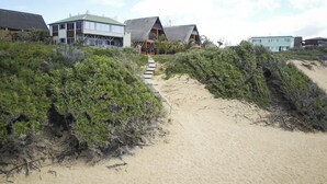 Un sentier sablonneux mène à un bâtiment dont le toit est recouvert de chaume, le tout étant entouré d’une végétation luxuriante.