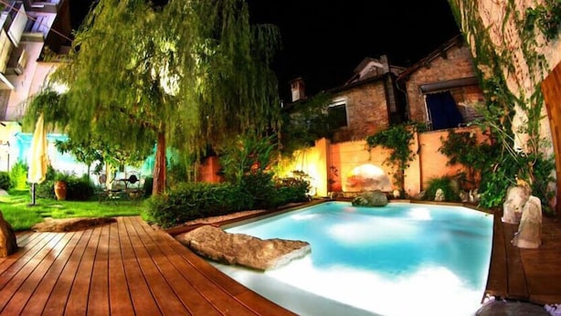 A swimming pool with a wooden deck, surrounded by greenery and stone features. - Lori's Inn (Mondovi)