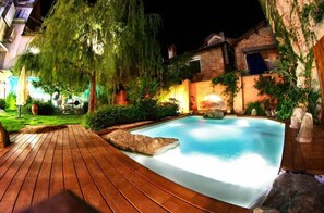 A swimming pool with a wooden deck, surrounded by greenery and stone features. - Lori's Inn (Mondovi)