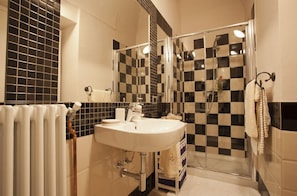 A bathroom with a checkered tile wall, a white sink, and a glass shower enclosure. - Lori's Inn (Mondovi)