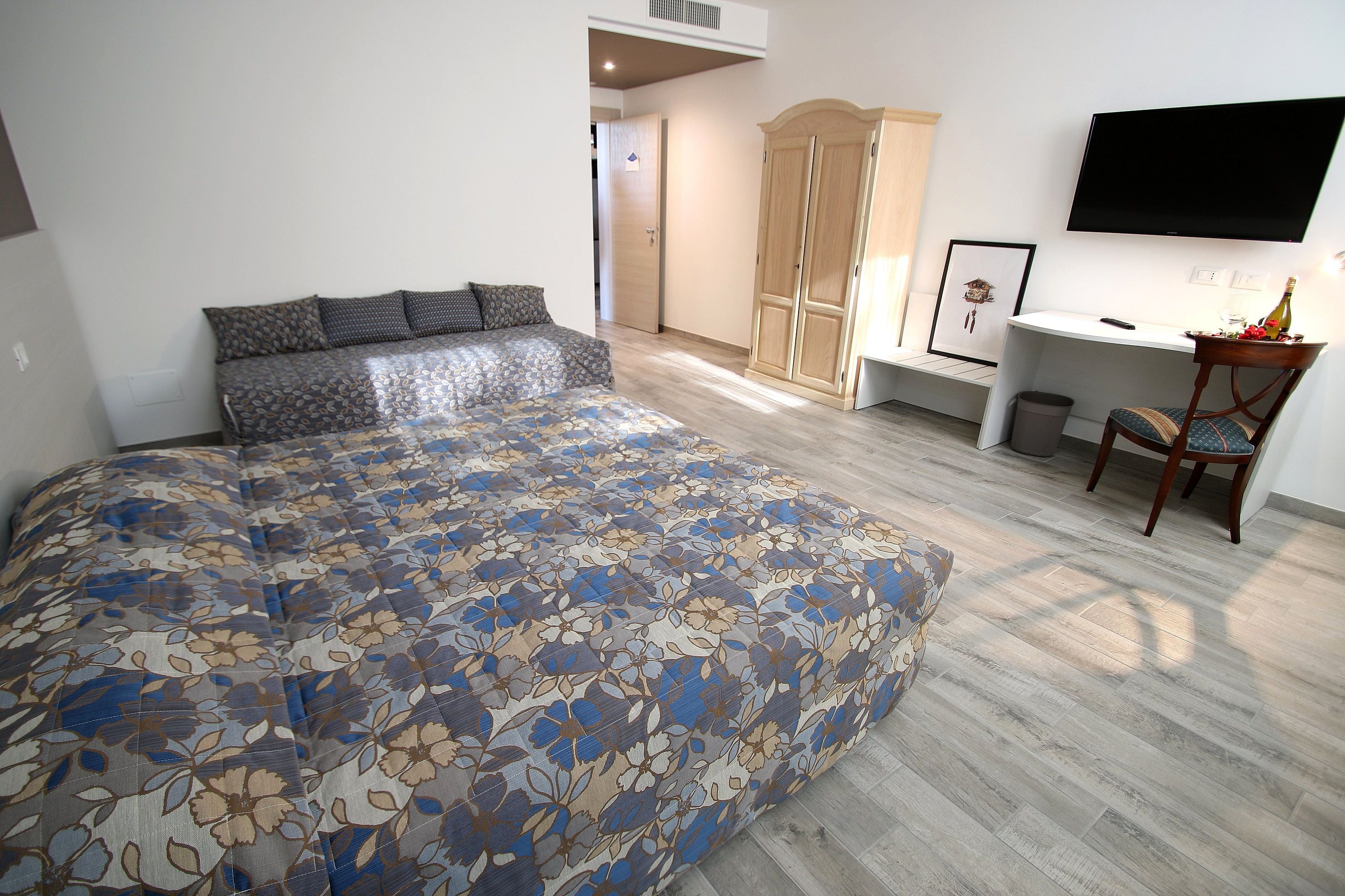 Ein Schlafzimmer mit einem großen Bett, einem Holzschrank, einem Schreibtisch mit Stuhl und einem an der Wand montierten Fernseher.