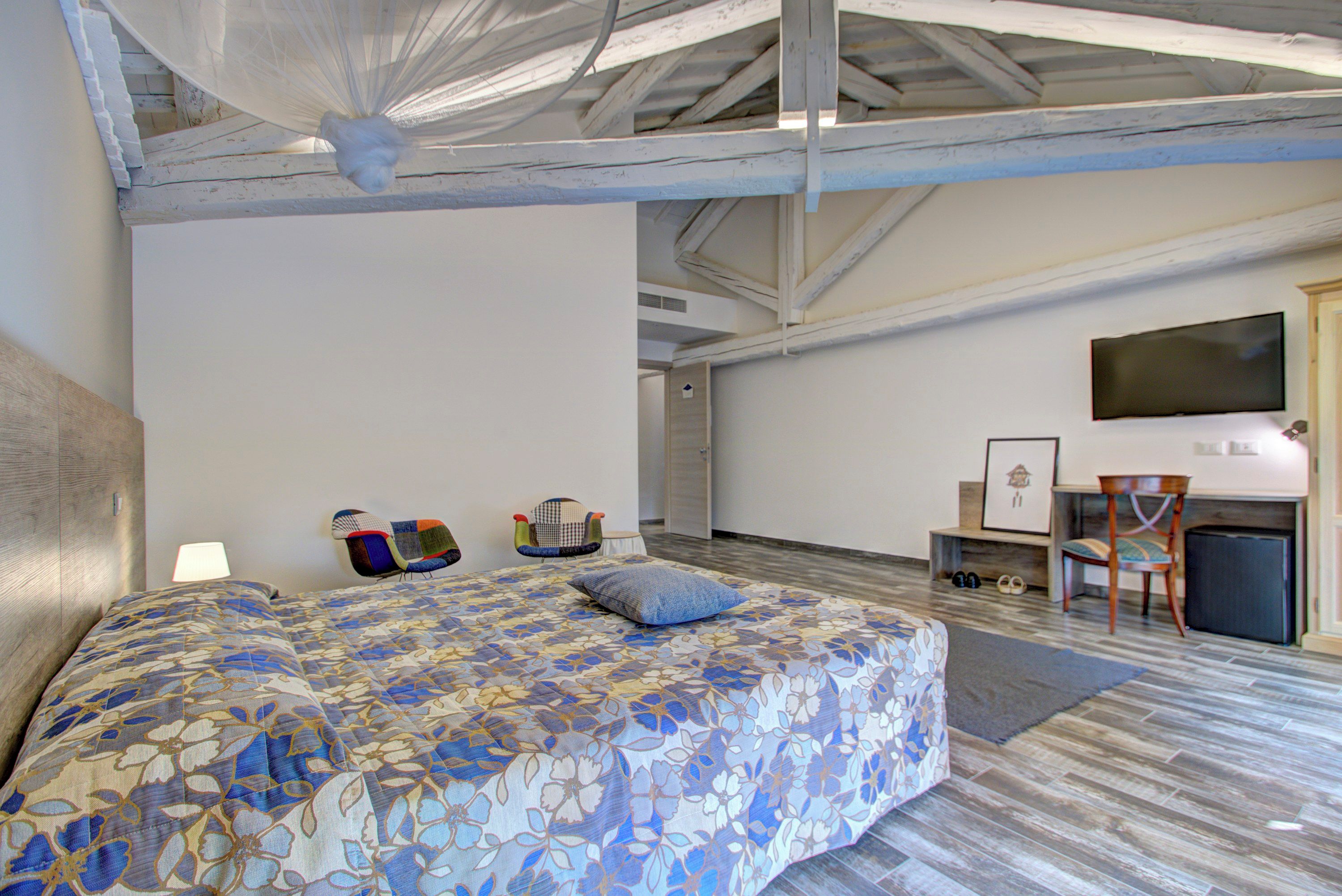 A bedroom with a large bed, a desk with a chair, a television, and a small cabinet.