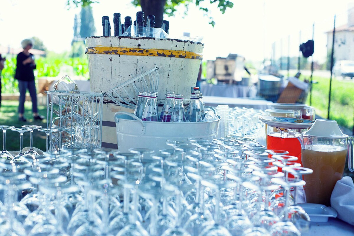 Una mesa con numerosos vasos de vino vacíos y un cubo de hielo grande con botellas.
