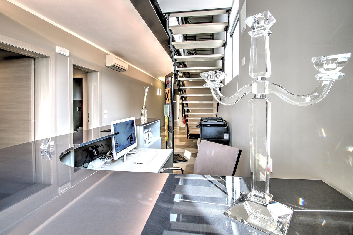 Una habitación de hotel moderna con un separador de vidrio, un escritorio con computadora, una silla y una escultura de vidrio decorativa.