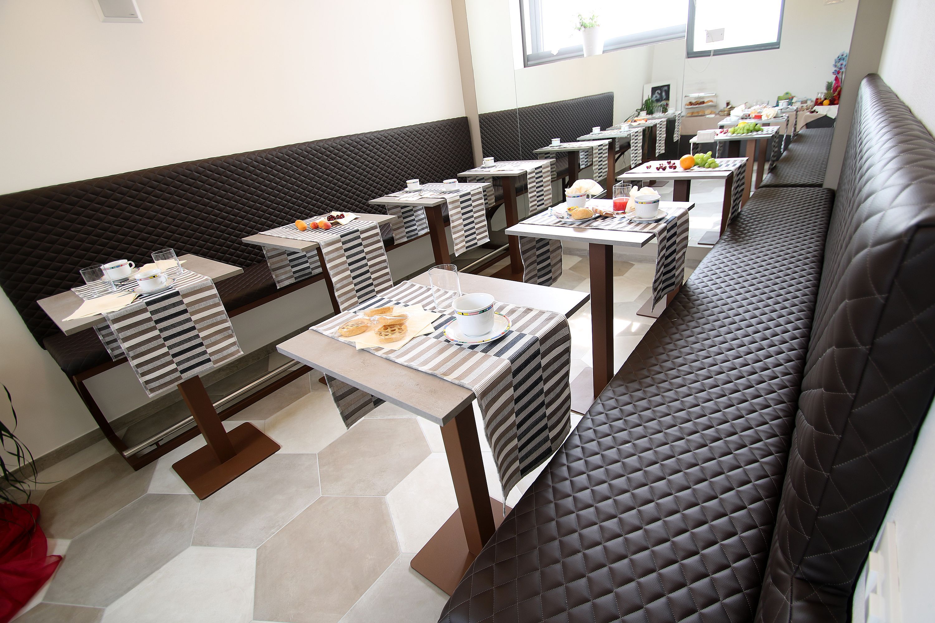 A restaurant with multiple tables and booths, each with a striped tablecloth and a variety of food items.