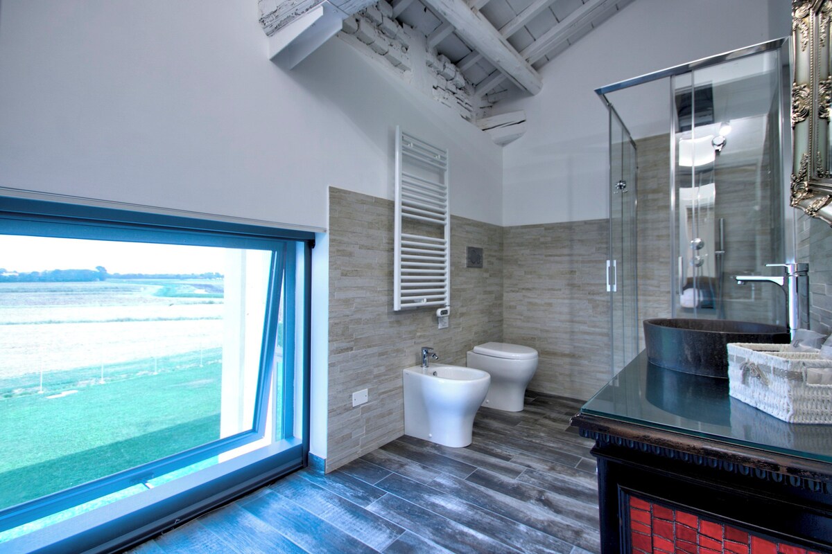 Un baño moderno con un ventanal amplio, un bidé, un inodoro y una cabina de ducha de vidrio.
