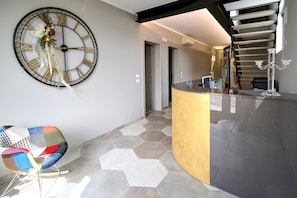 A modern interior with a large wall clock, a unique seating area, and a staircase. - Resilienza (Mira)