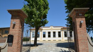 A gated entrance with a stone pathway leading to a building with a tiled roof and multiple windows. - Resilienza (Mira)