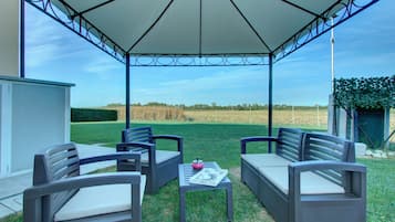 Un patio al aire libre con dos sofás grises y una mesa, un paraguas blanco y vistas a un campo.