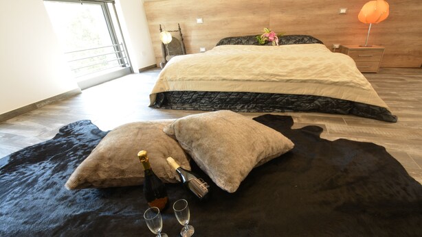 A bedroom with a large bed, a nightstand with a lamp, and a window with a view of greenery. - Resilienza (Mira)