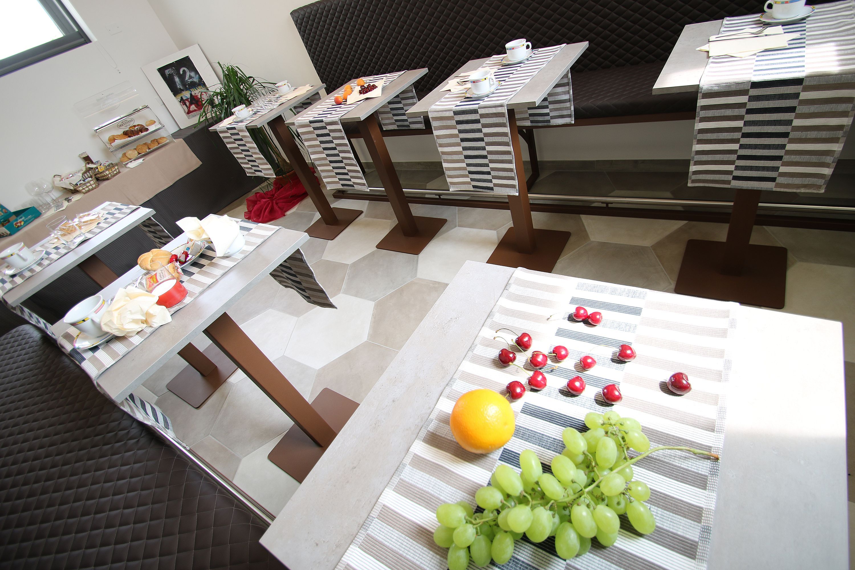 Un espace repas avec des tables préparées pour le petit-déjeuner, où l’on trouve des fruits et des viennoiseries.