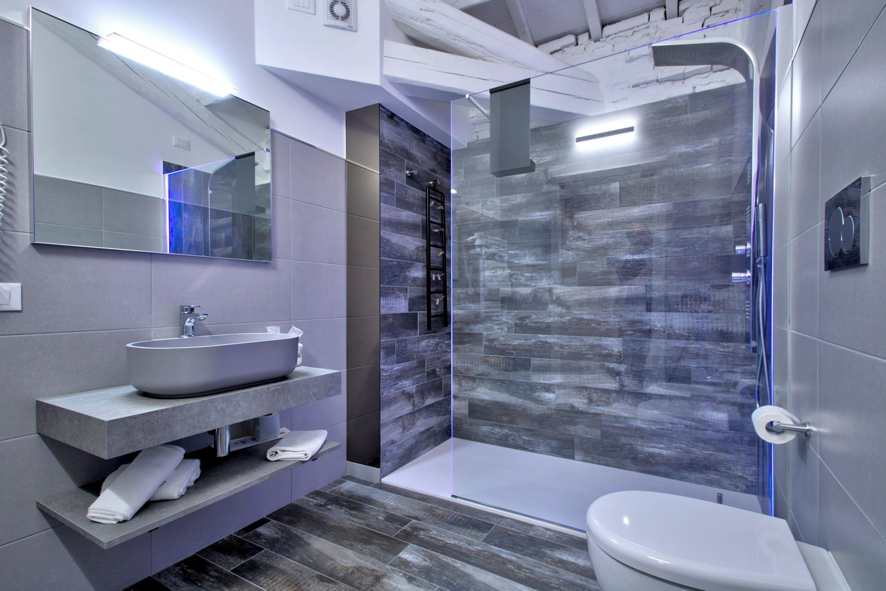 Un baño moderno con un espejo grande, un lavamanos, un inodoro y una ducha con mampara de vidrio.