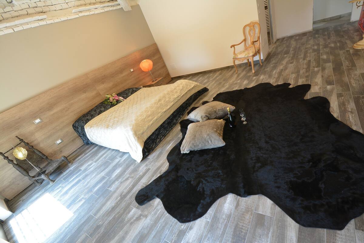A room with a bed, a black fur rug, and a wooden floor.