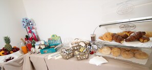 Una mesa con diversas opciones de comida, incluyendo pasteles y frutas, junto a una vitrina con más pastelería.