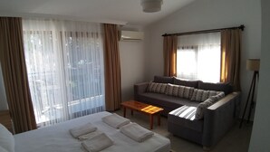 A hotel room with a bed, a sofa, a coffee table, and large windows with curtains.