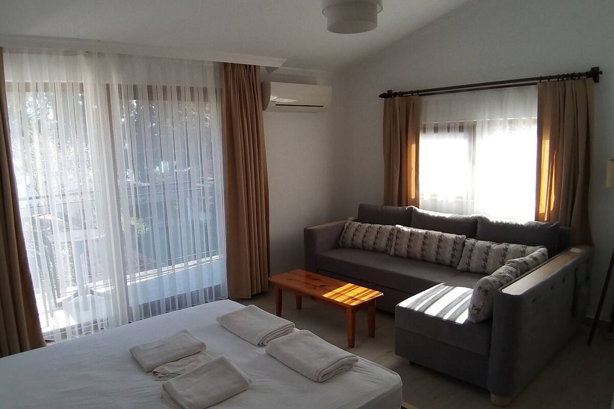 A hotel room with a bed, a sofa, a coffee table, and large windows with curtains.