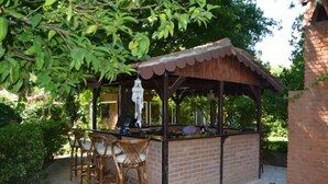 An outdoor bar area with a brick counter, wicker chairs, and a wooden pergola.