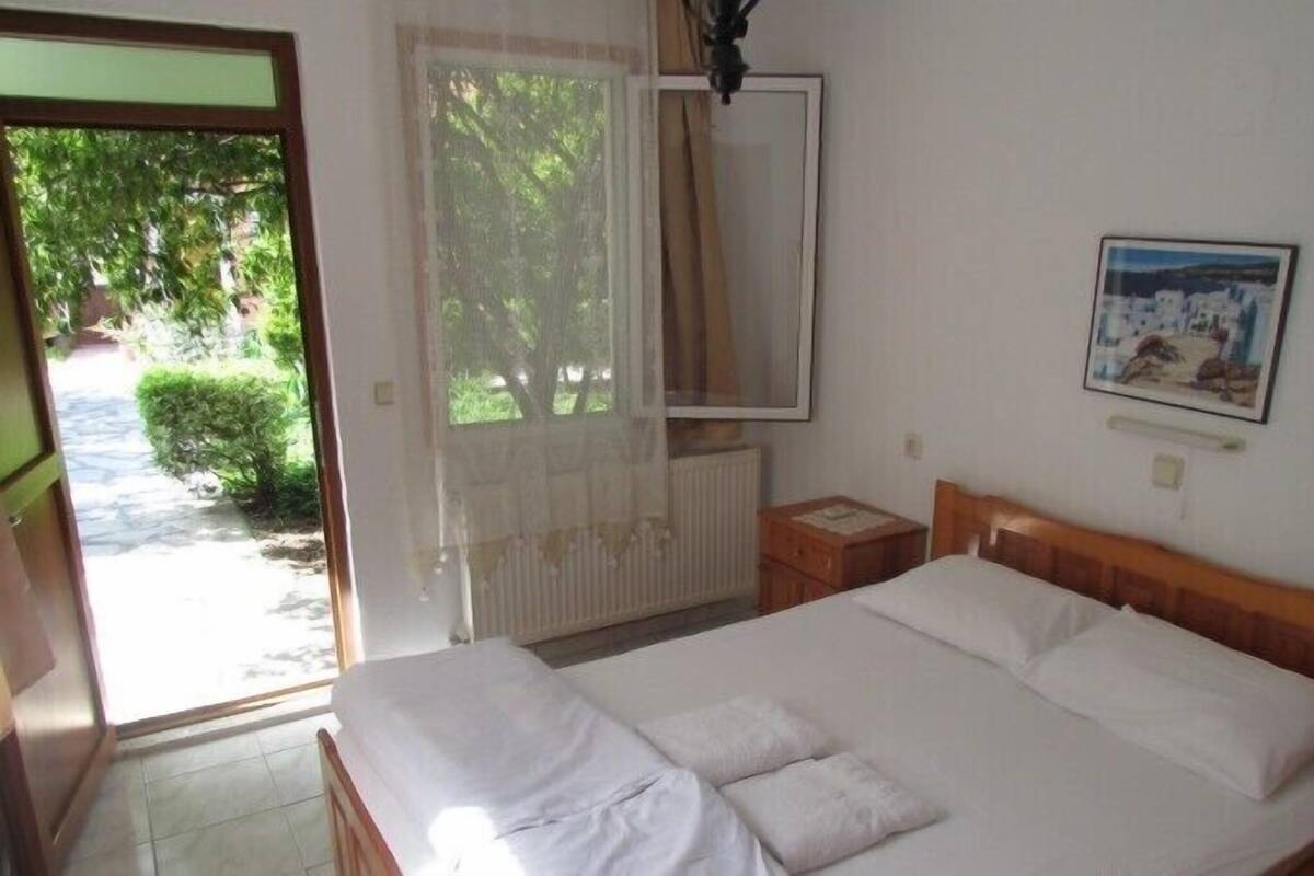 A bedroom with a bed, a window with curtains, a radiator, a bedside table, and a framed picture on the wall.