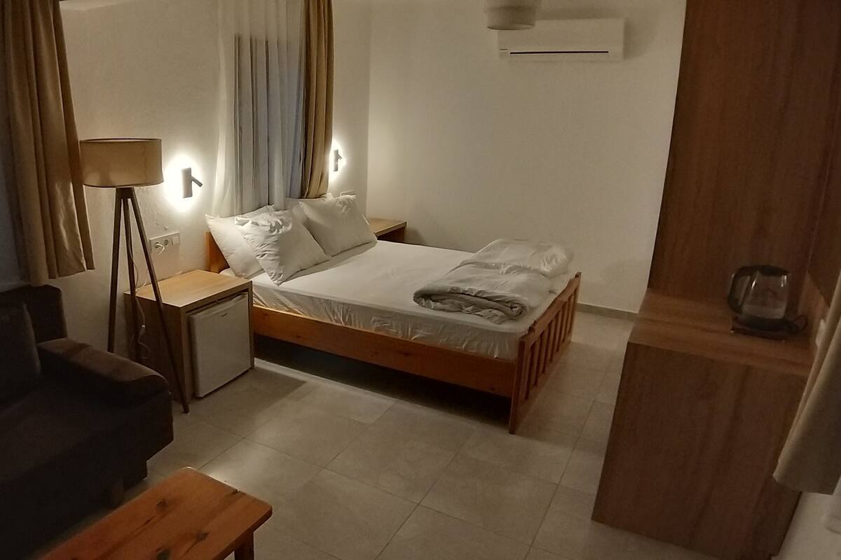 A compact hotel room with a single bed, a small bedside table, a desk, a chair, and a lamp.