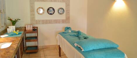 A spa room with a massage table, a sink, and a shelf with toiletries.