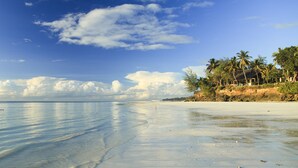 A beach with clear water, palm trees, and a structure on the shore.