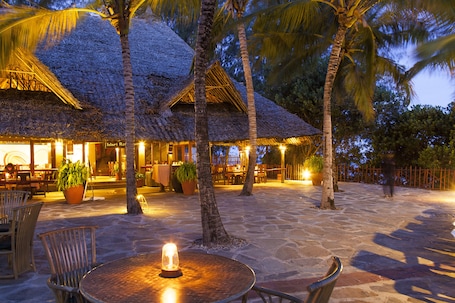 A restaurant with thatched roofs, outdoor seating, and palm trees.