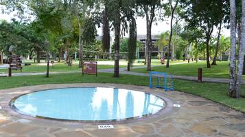 Uma piscina circular com borda de pedra, rodeada por um espaço gramado com árvores e uma cerca azul.