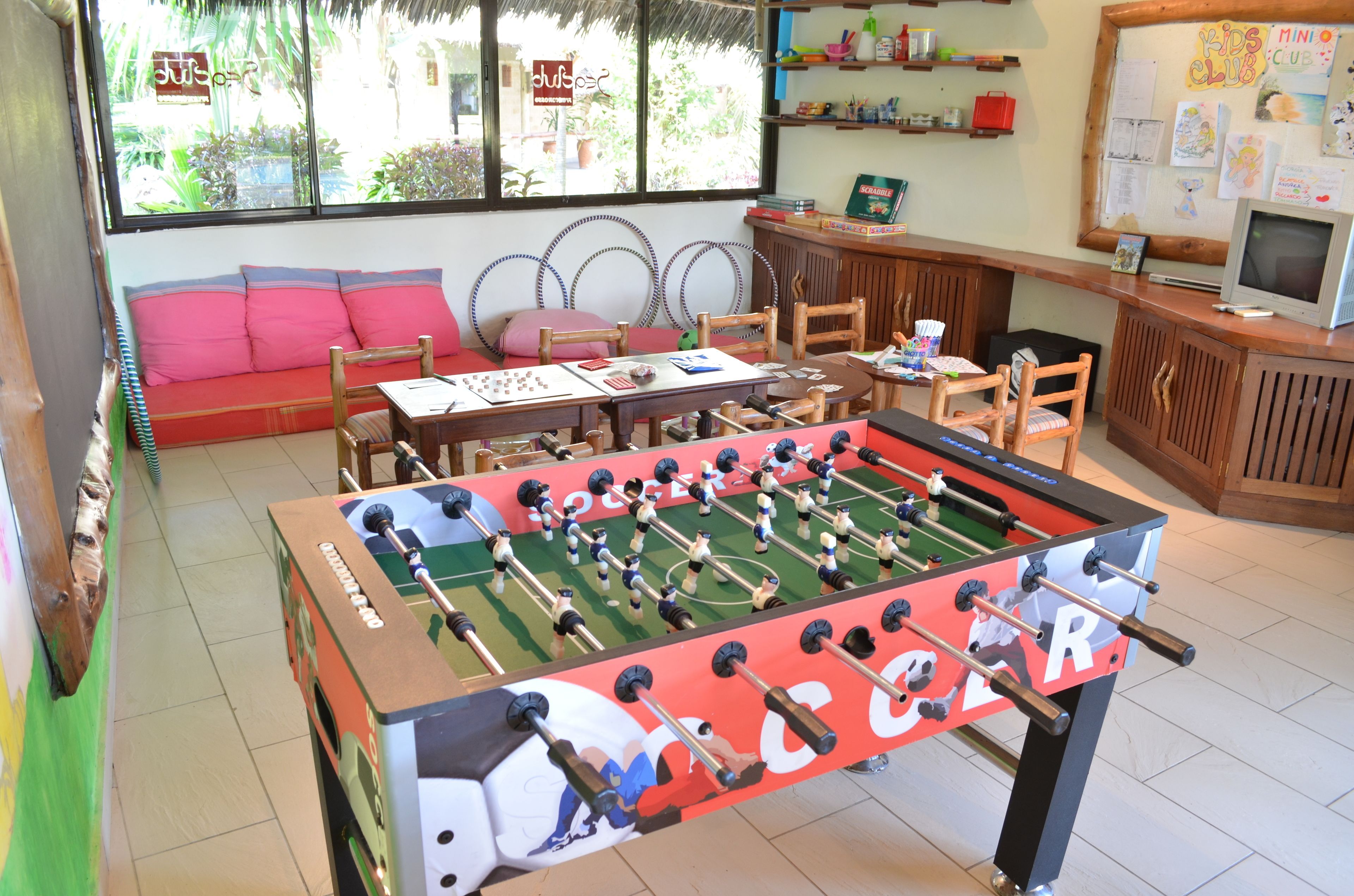 A room with a foosball table, a sofa, a table with chairs, and a TV.