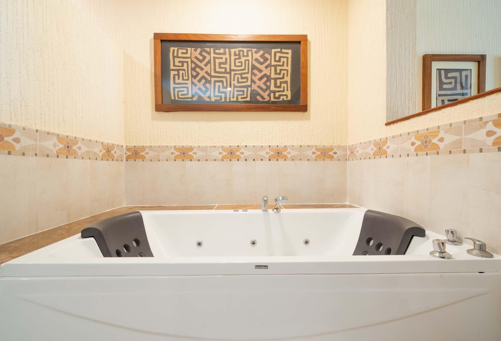 A modern bathroom with a large bathtub, decorative wall tiles, and a framed artwork above the tub.