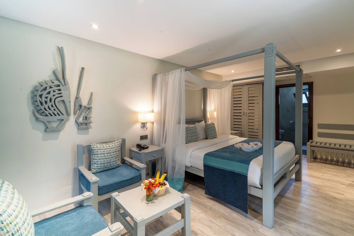 Un dormitorio moderno con cama con dosel, un rincón de estar con una silla y una mesa, y un adorno de pared decorativo.