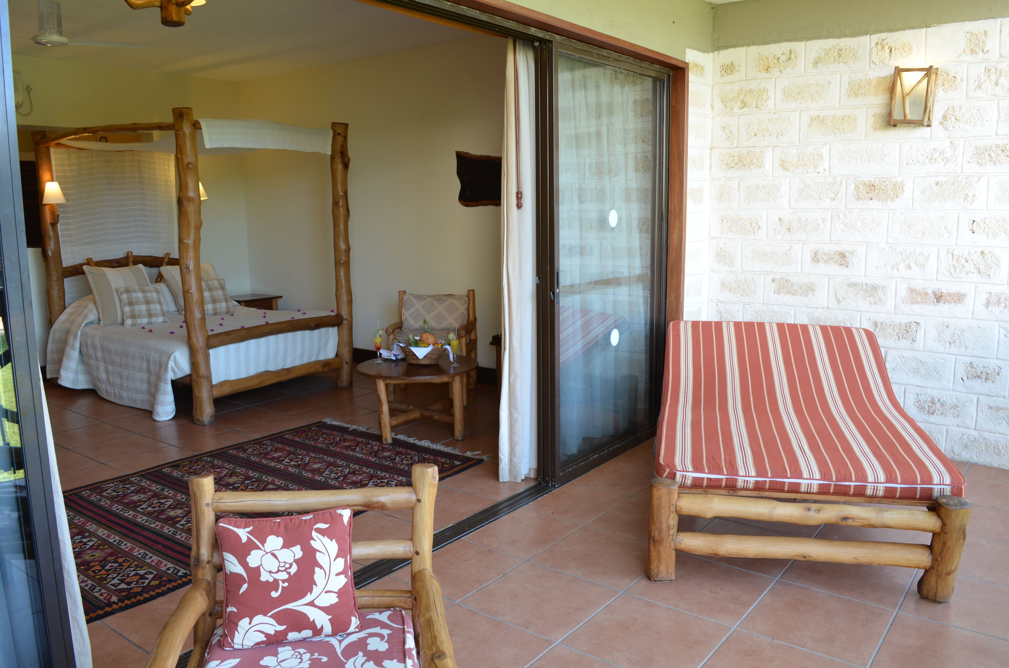 A room with a bed, a wooden chair, a table with fruit and drinks, and a red-striped sofa.