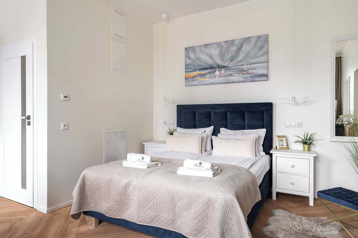 Quarto moderno com cama grande, cabeceira, mesas de cabeceira, mesa de apoio, pintura e espelho.