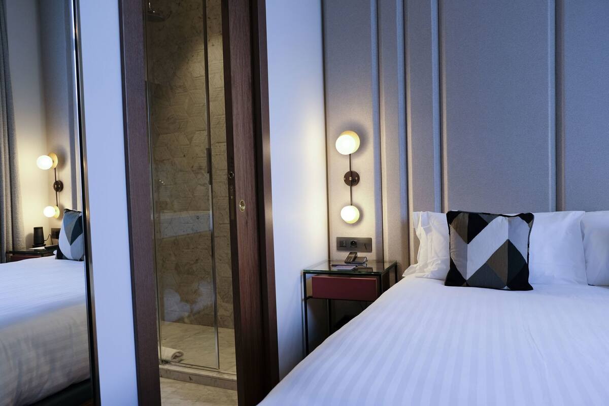 A hotel room with a bed, a nightstand, a mirror, and a shower area.